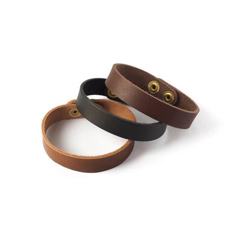 Hình ảnh cận cảnh quy trình làm vòng tay handmade từ dây da, với keo dán và dụng cụ đục lỗ.