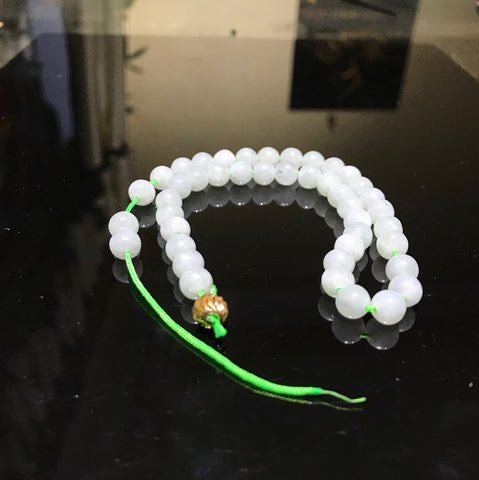 Một chiếc vòng tay đá tự nhiên màu xanh ngọc bị đứt, các hạt đá vương vãi trên nền gỗ.