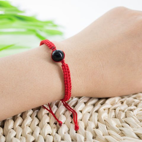 Một người đang tết vòng tay handmade bằng sợi chỉ đỏ may mắn, tập trung vào từng nút thắt tỉ mỉ.